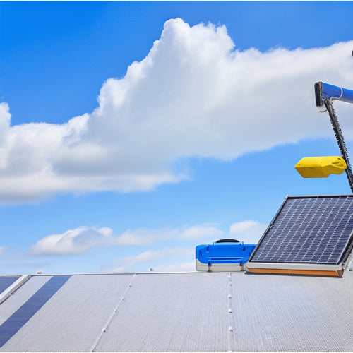 A bright blue sky with fluffy white clouds, a rooftop with a solar panel array, and a toolbox with a wrench, pliers, and cables, surrounded by a subtle grid pattern in the background.